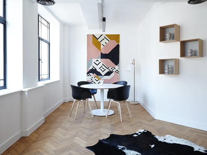 Salón vacío con suelo de espiga, molduras y una mesa redonda junto a la ventana