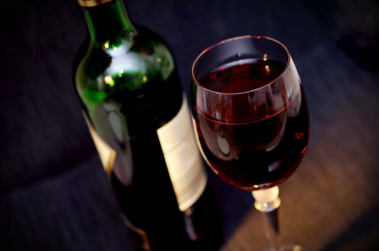 Botella de tinto y copa servida sobre una mesa de madera, con luz baja