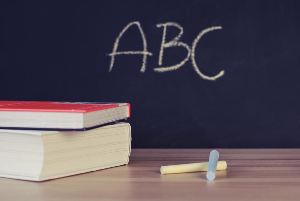 Libros apilados y tizas sobre una mesa de madera delante de una pizarra con las letras ABC, imagen ilustrativa