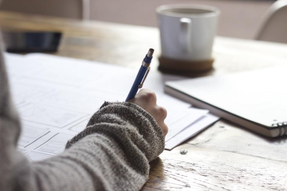 Manos escribiendo con lápiz sobre una mesa de madera, imagen ilustrativa