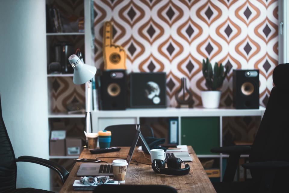 Escritorio de estudio con flexo, altavoces y una taza, frente a una pared empapelada con formas geométricas