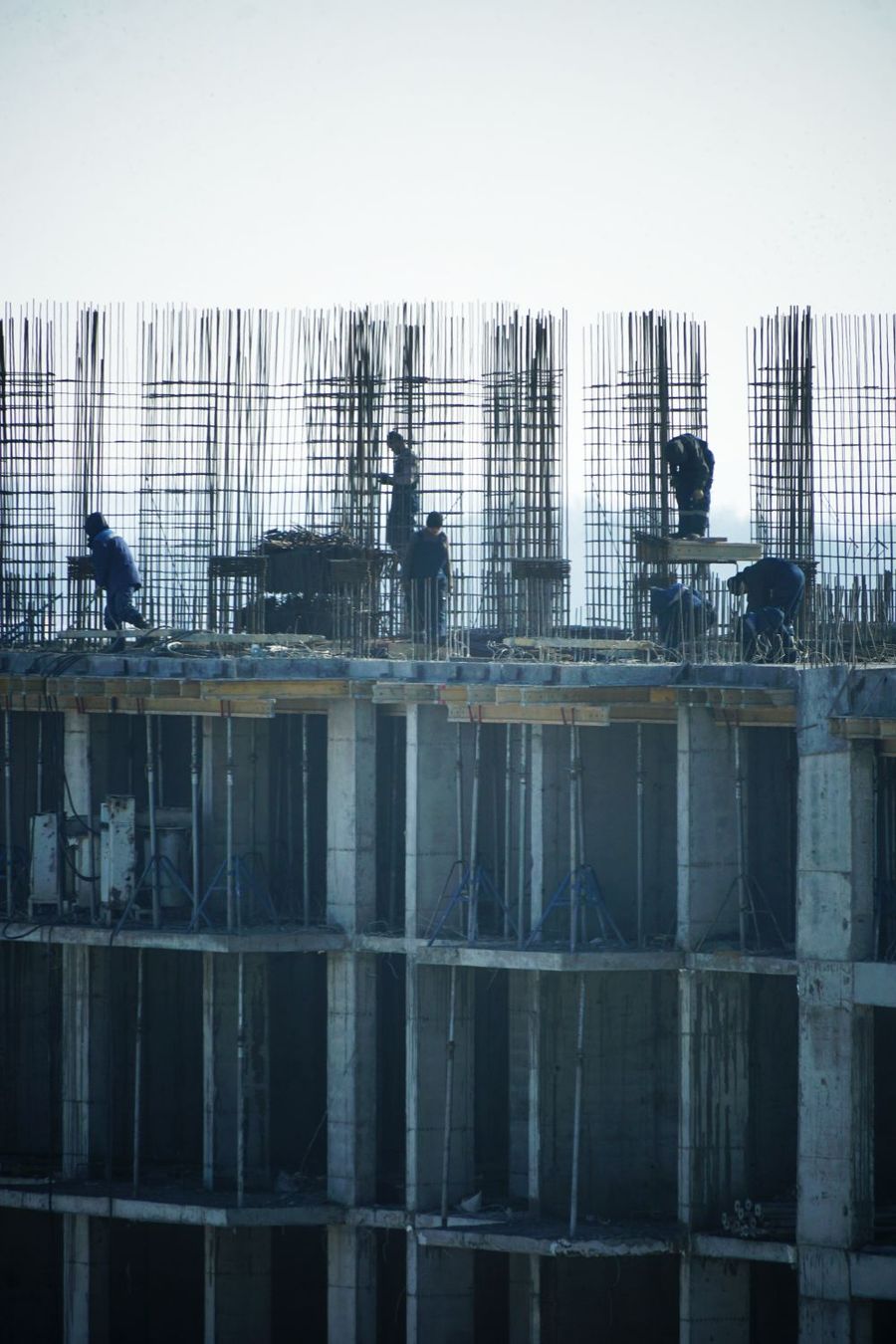 Estructura de hormigón de un edificio en construcción, con las esperas de acero de los pilares y operarios trabajando sobre el último forjado