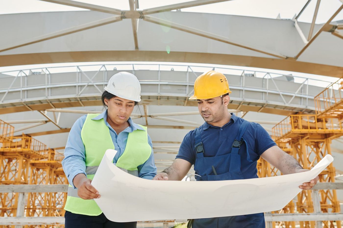 Dos técnicos con casco revisando sobre el terreno los planos desplegados de una obra