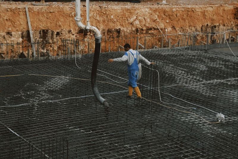 Manguera de la bomba de hormigón apoyada sobre la ferralla de una losa de cimentación, con un operario cruzando la malla