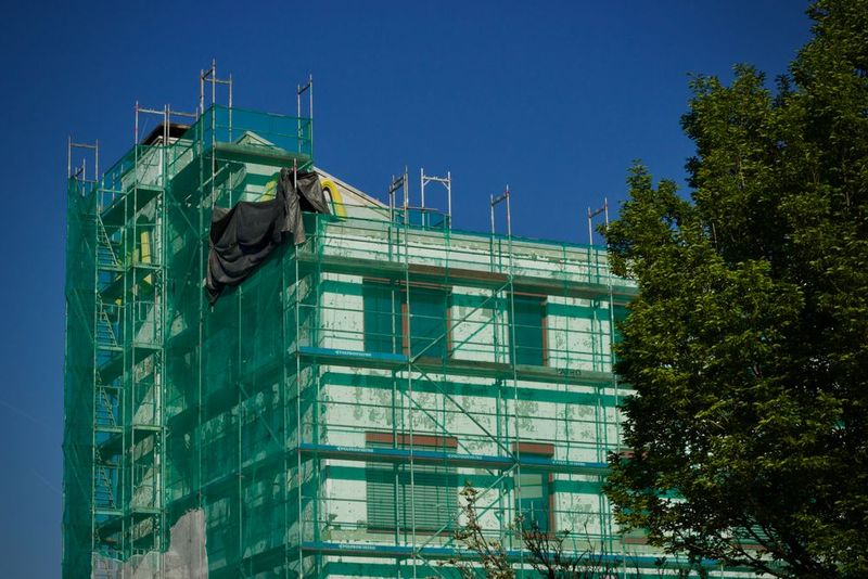 Fachada de un edificio de viviendas cubierta con andamio y malla verde durante una rehabilitación