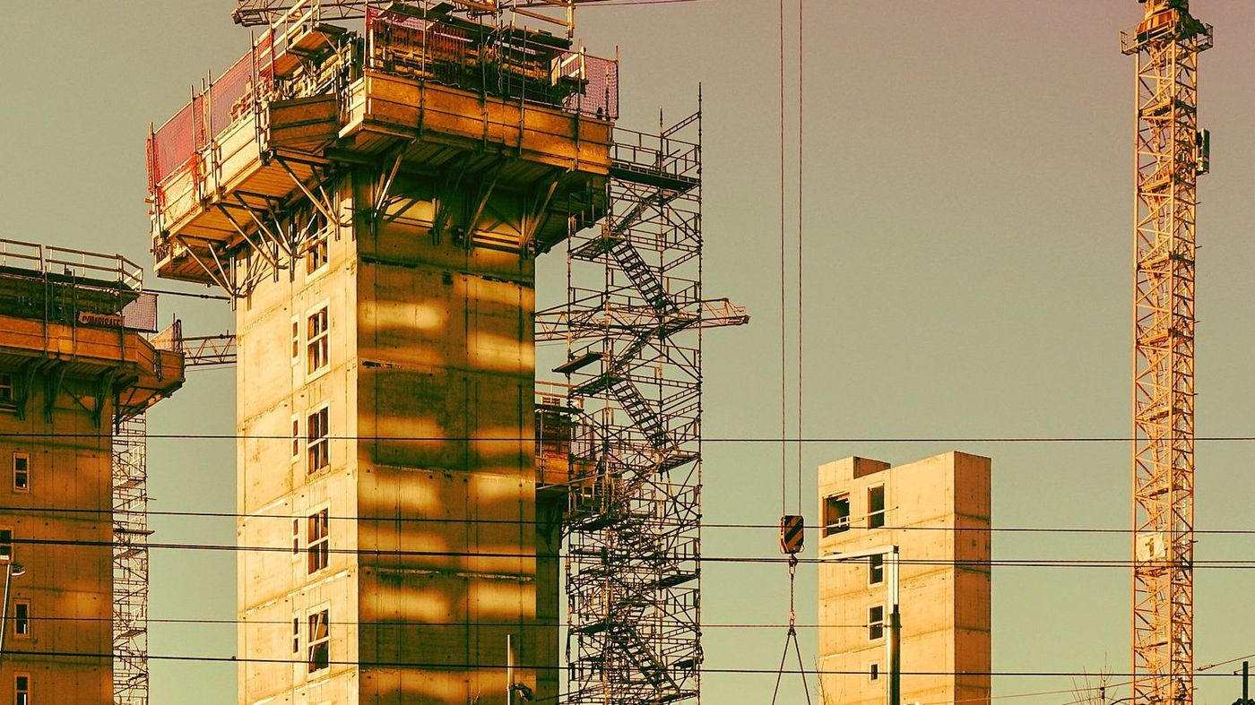 Edificio en construcción al atardecer, con encofrado en la coronación, torre de andamio de escalera y dos grúas torre