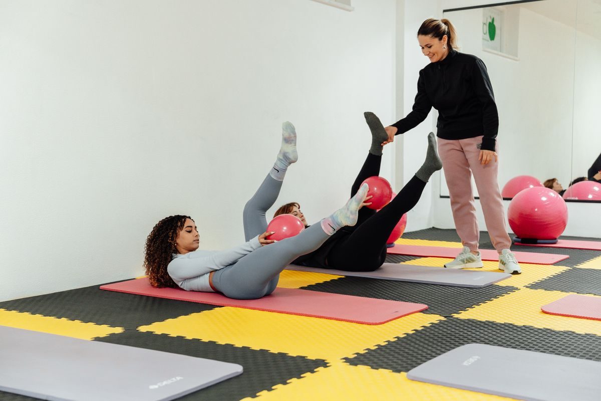 Clase dirigida en Terne: dos socias haciendo abdominales con balón mientras la entrenadora les sujeta los pies